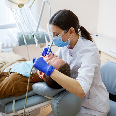 A female dentist treats tooth decay on a male patient's teeth at a dental clinic during the coronavirus pandemic. Selective focus